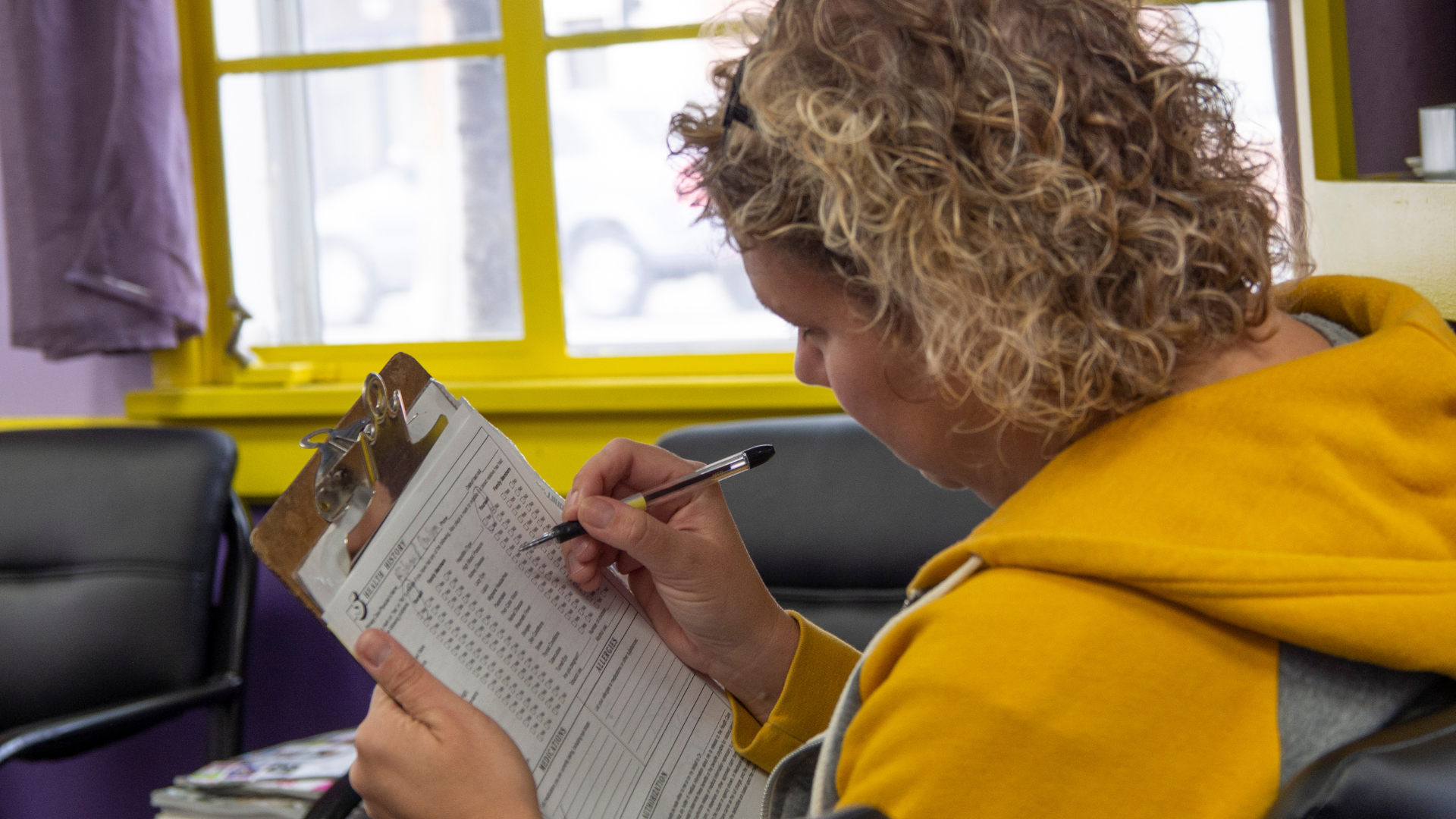 A woman with curly hair filling out a form on a clipboard
